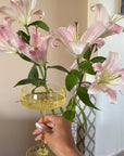 Hand holding a Summer Yellow coupe glass beside pink lilies