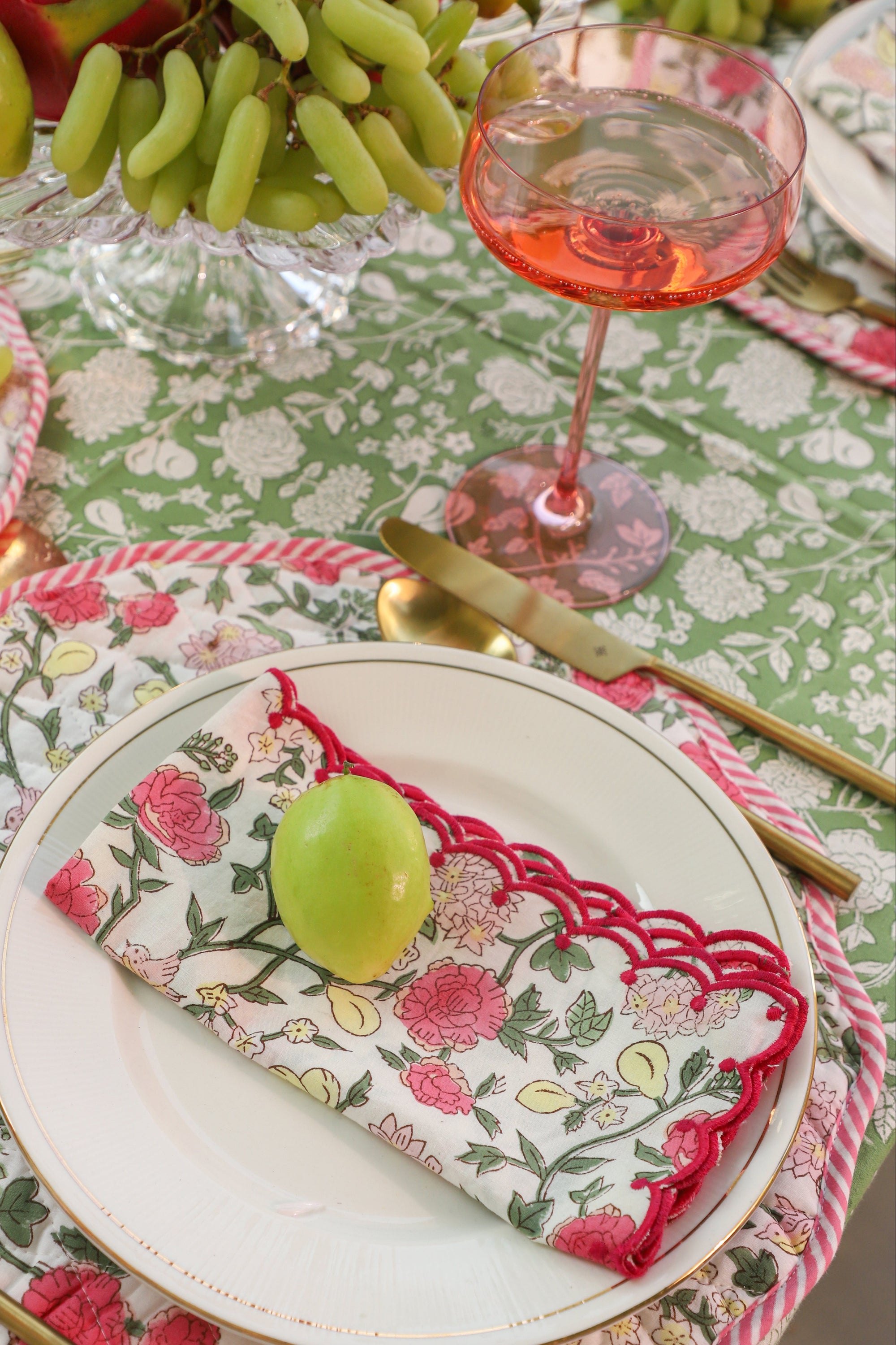 Dining table setting with floral tablecloth, plates, cutlery, and fruit.
