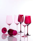 Six pink and magenta tinted wine glasses arranged on a glossy white reflective surface against a white studio background.