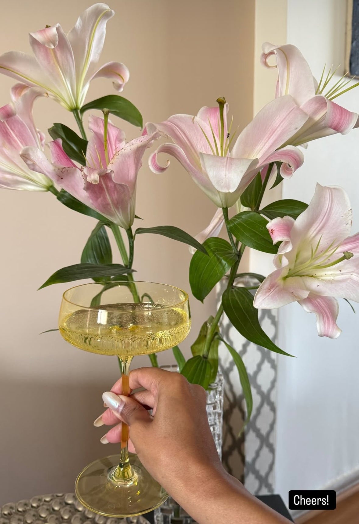 Hand holding a Summer Yellow coupe glass beside pink lilies